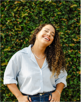 Poliane sorrindo em frente a um muro verde